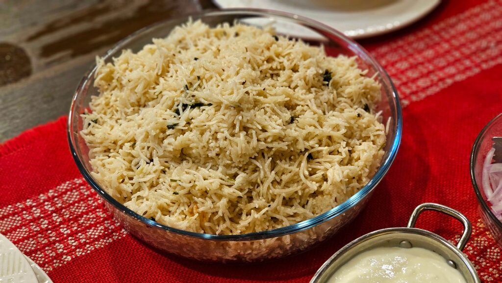 A bowl of perfectly cooked basmati rice served with yogurt on a red tablecloth.